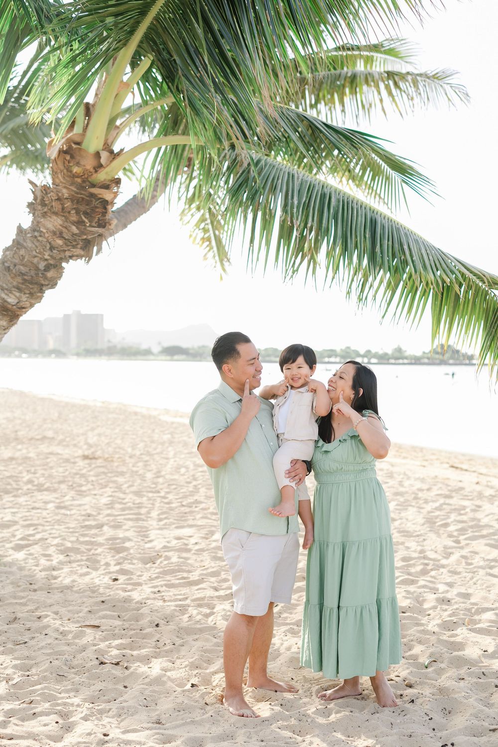A couple in mint green and white outfits share romantic moments on a tropical beach under swaying palm trees.