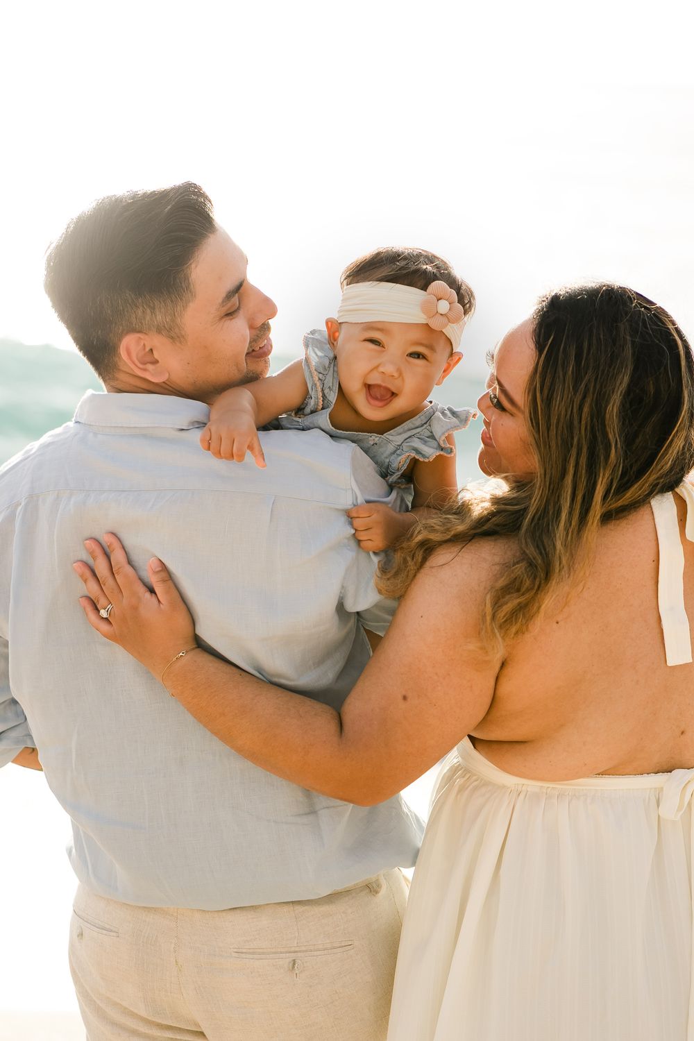 A loving family in white clothing embraces and laughs together against a bright background.