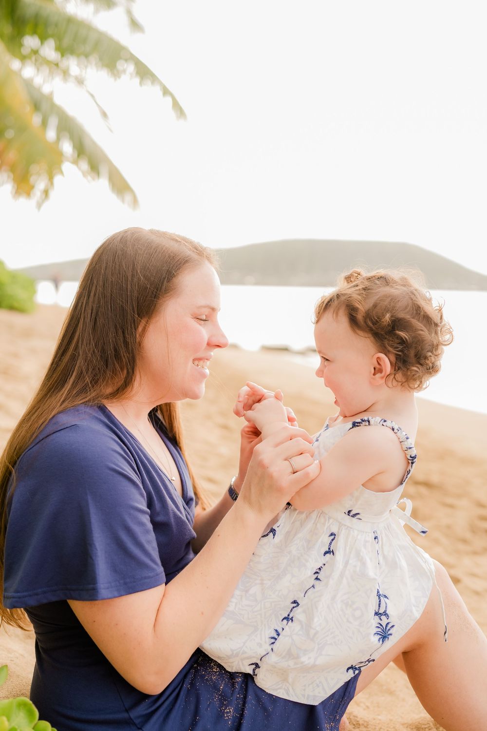 A parent and child share a tender moment playing together on a sunny beach.