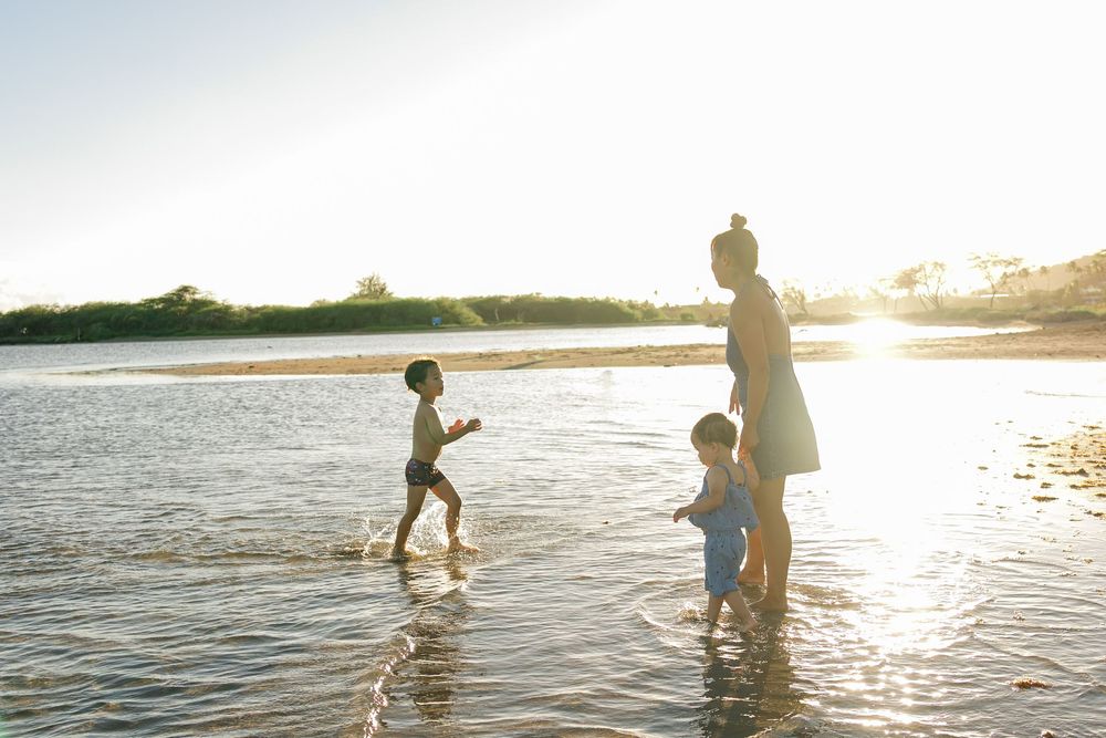 Family enjoying a playful moment together in shallow ocean water at sunset with golden light reflecting on waves.