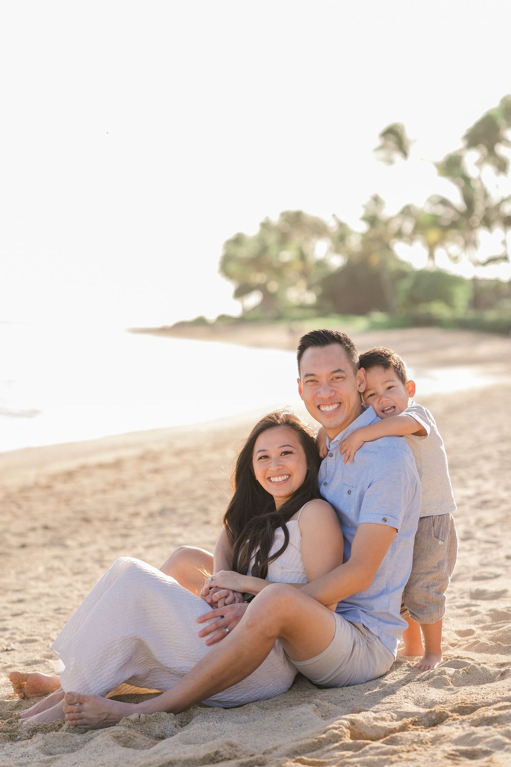 Family enjoying a relaxing moment together on a sandy beach with palm trees at sunset.