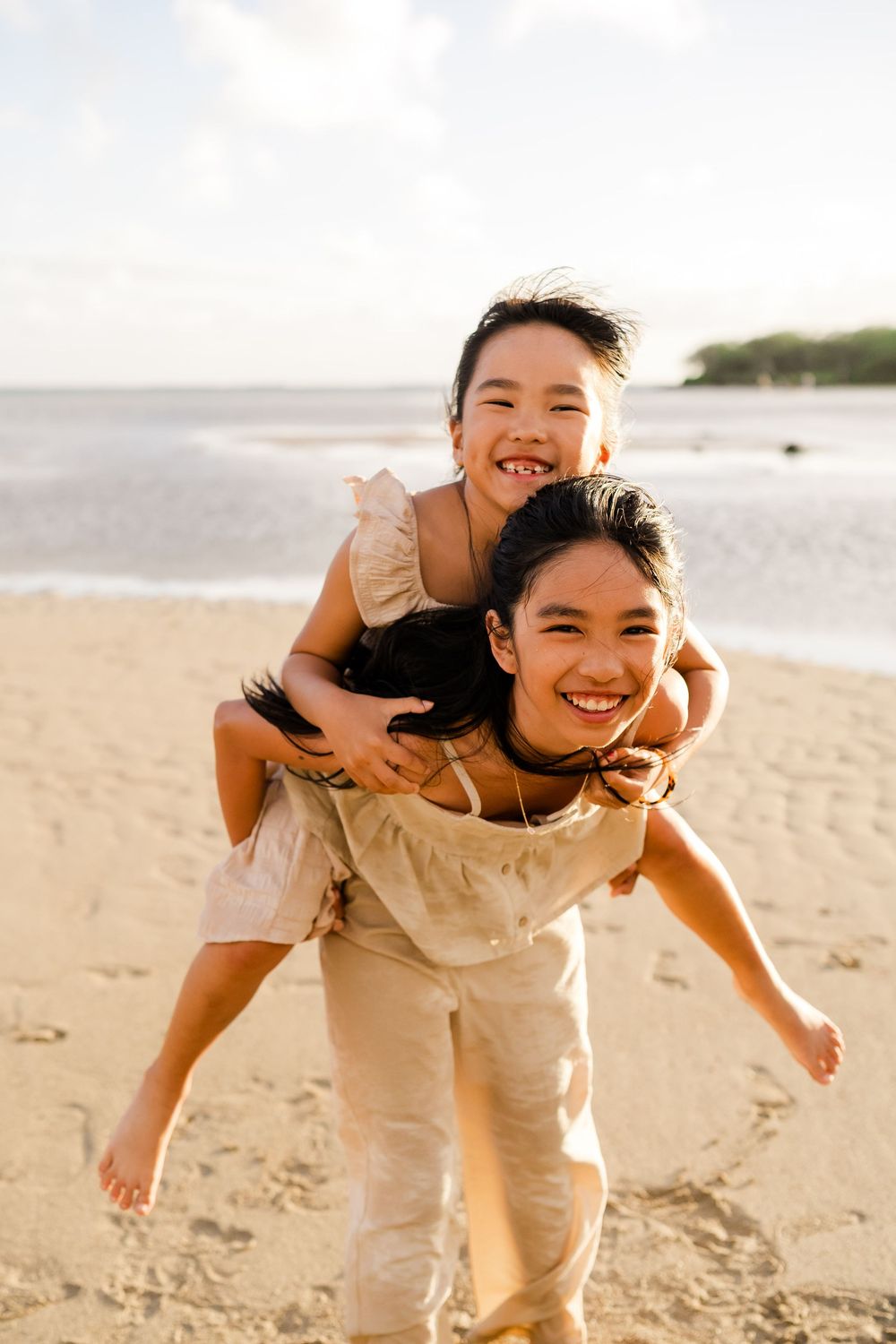 A joyful piggyback ride moment captured on a sunny beach with warm lighting and natural expressions.
