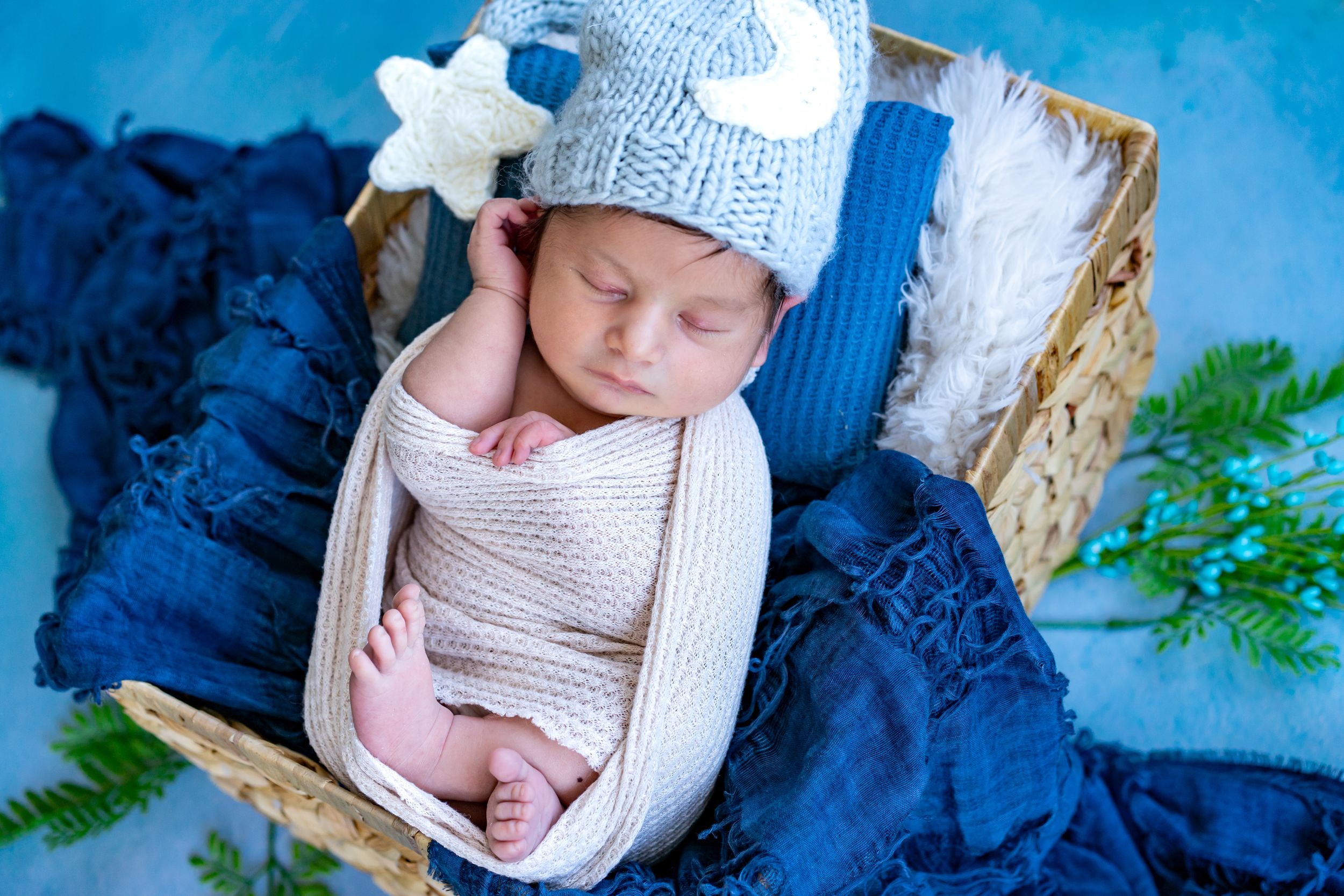 Peaceful newborn session featuring blue wraps and natural elements on light background.