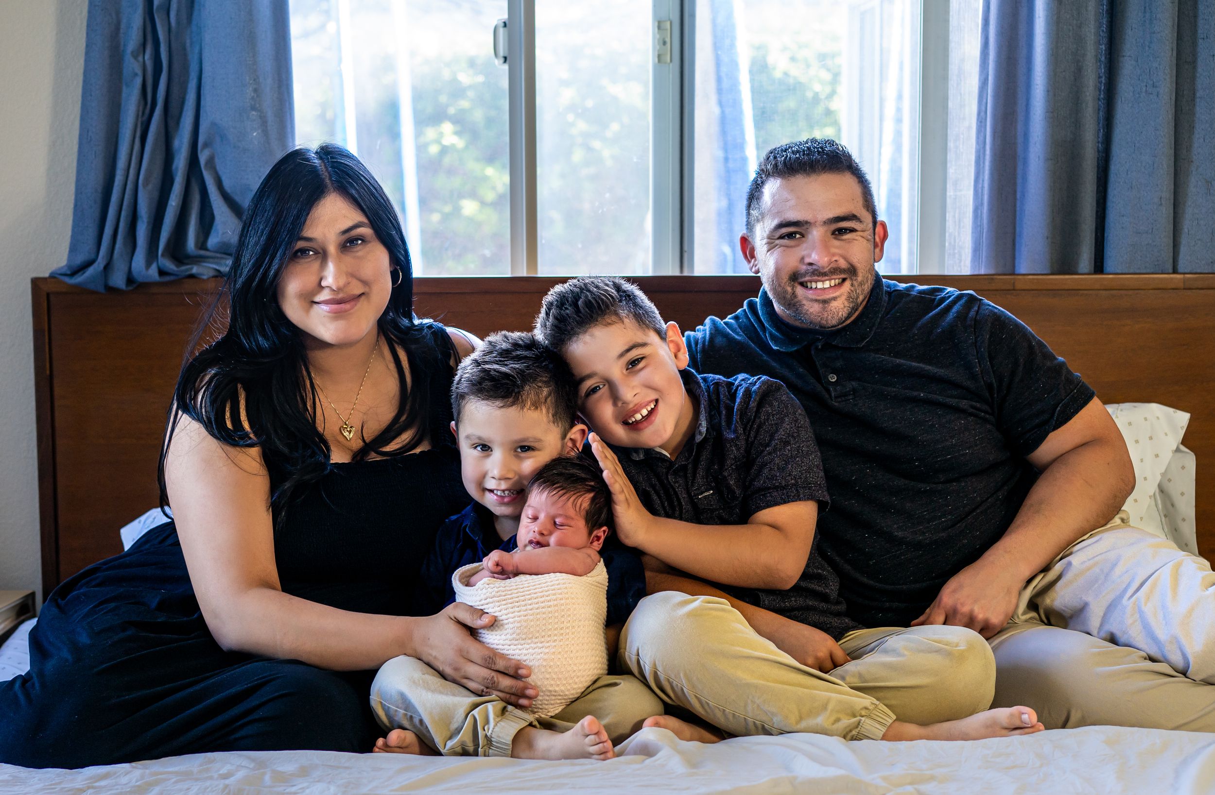Family members in dark clothing posing together on white bedding.