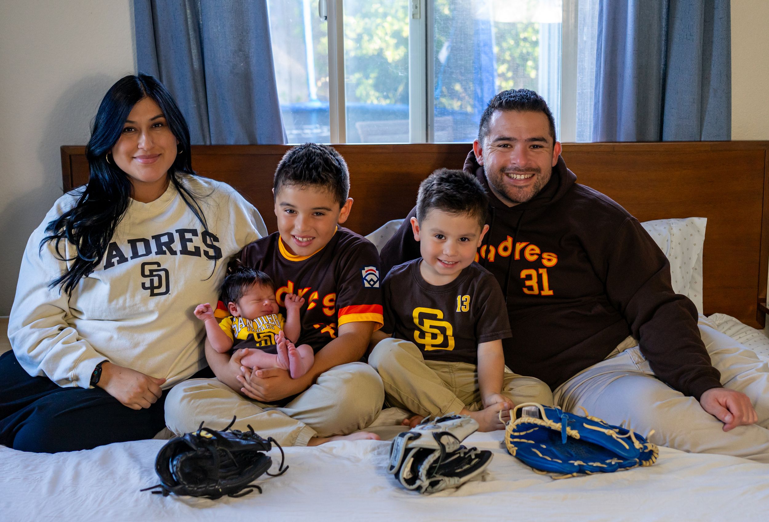 Family wearing San Diego Padres gear while relaxing on bed together.