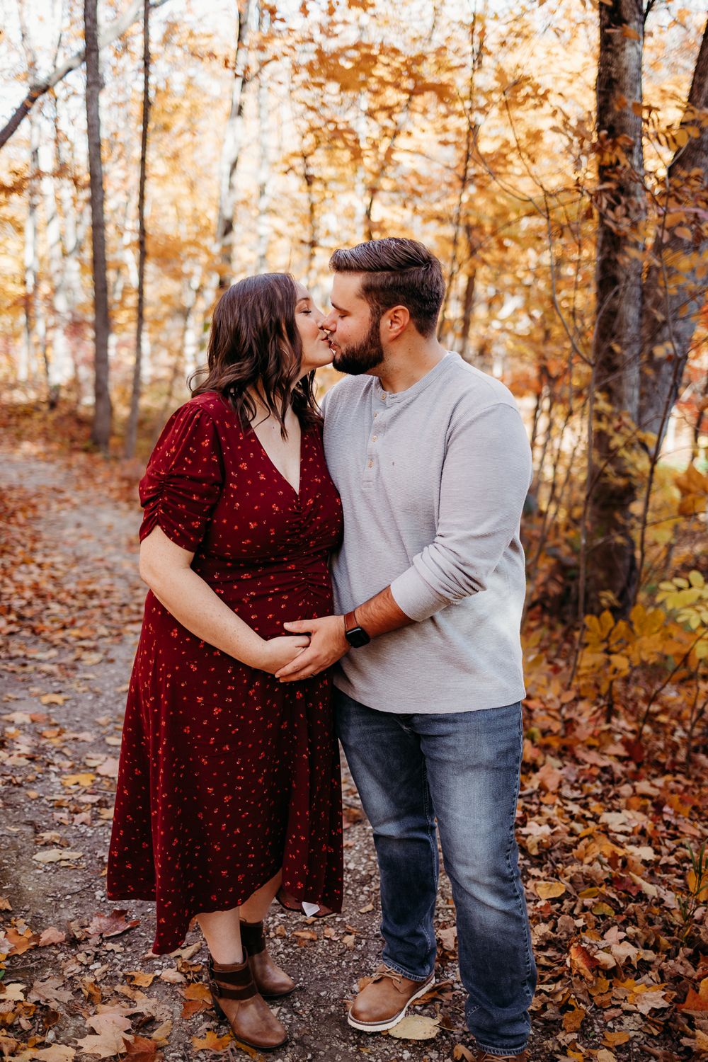 A couple standing each other and they are both holding each others hand on the expectant mothers belly.