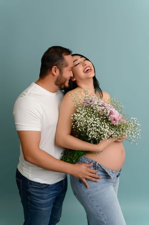 Romantic maternity photos with couple embracing and holding flowers against blue backdrop.
