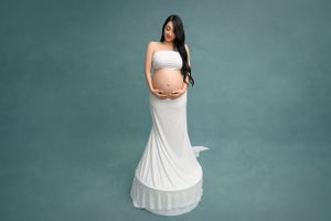 Elegant maternity photos featuring white pleated dress against turquoise backdrop.