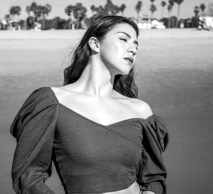 High-fashion Black and White image, young, long-haired brunette woman at sunny beach, eyes closed, puffy sleeved off the shoulder shirt