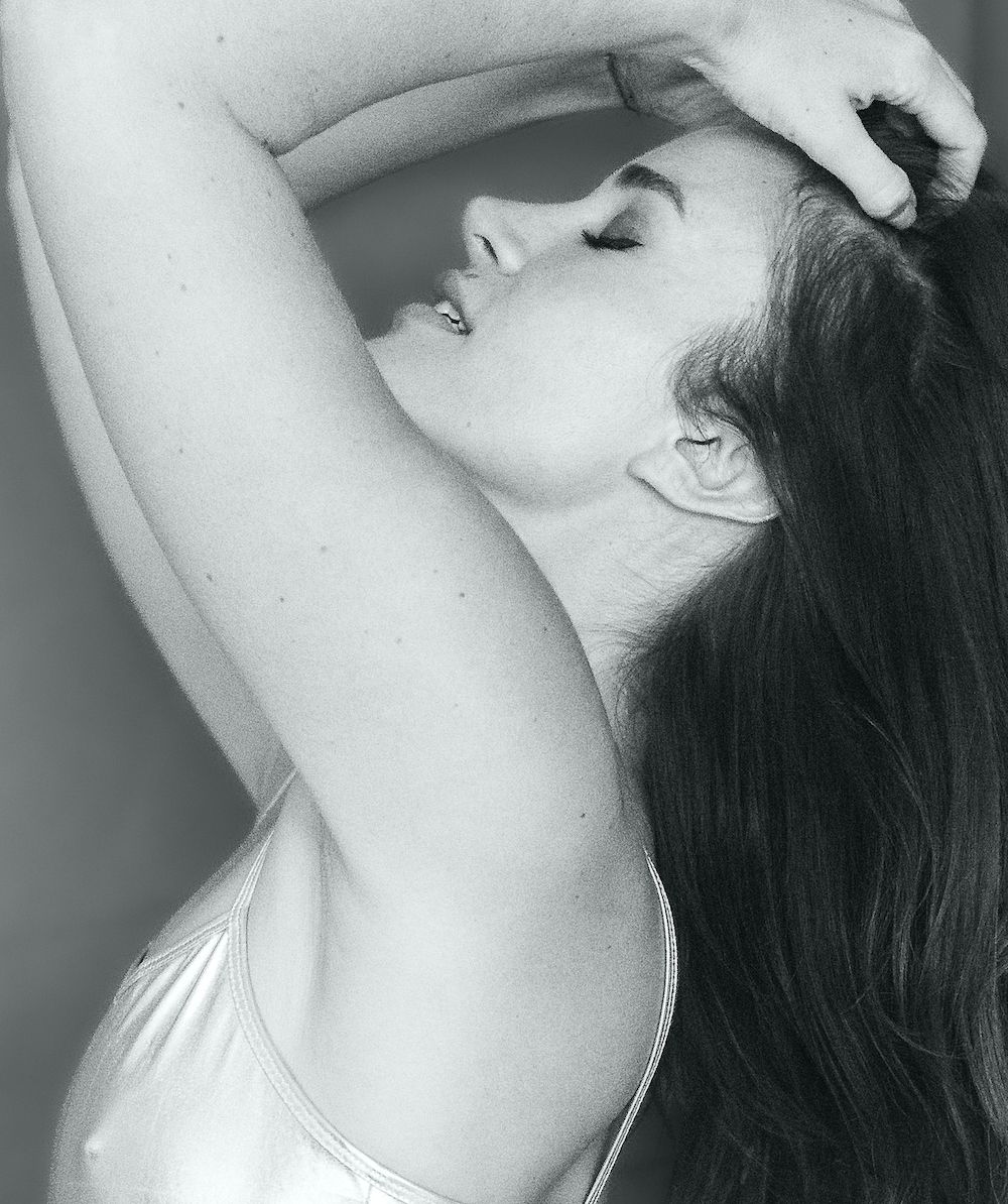 High-fashion Black and white profile portrait of young brunette woman in silver shirt with eyes closed, hands through hair, in pleasure.