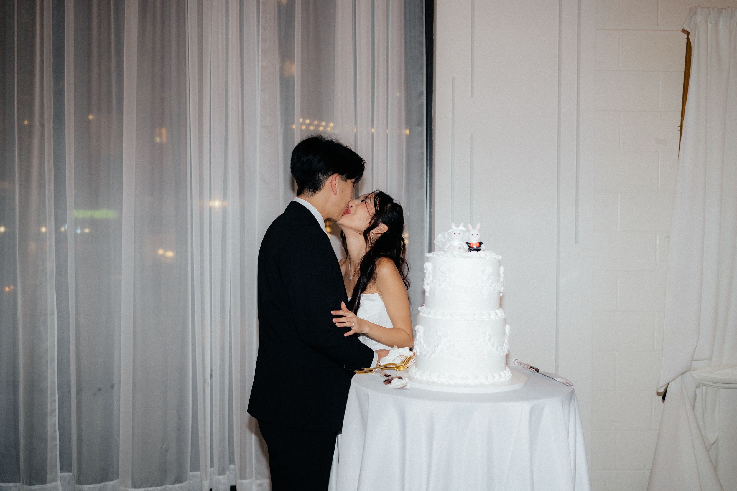 A couple shares a romantic moment while cutting their elegant white wedding cake at their reception.