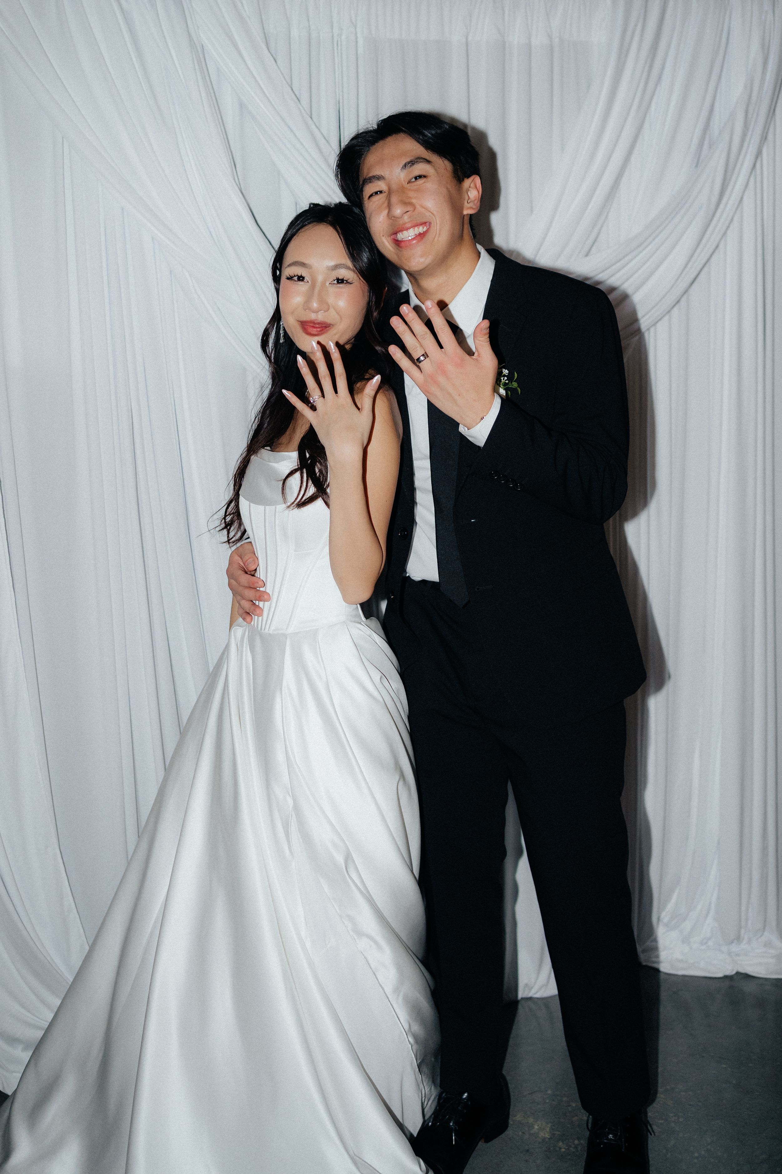 A couple in contrasting black and white formal attire poses playfully against a draped white backdrop in a photo series.