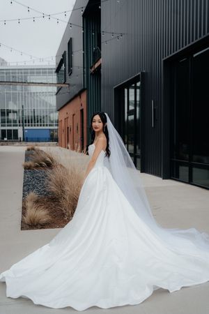 A flowing white wedding dress with a dramatic cathedral train photographed against an industrial building exterior.