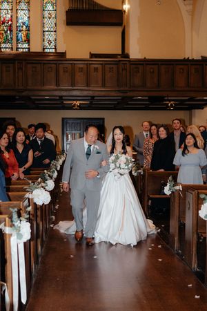 A wedding ceremony procession walking down the aisle of a traditional church with stained glass windows and wooden pews.
