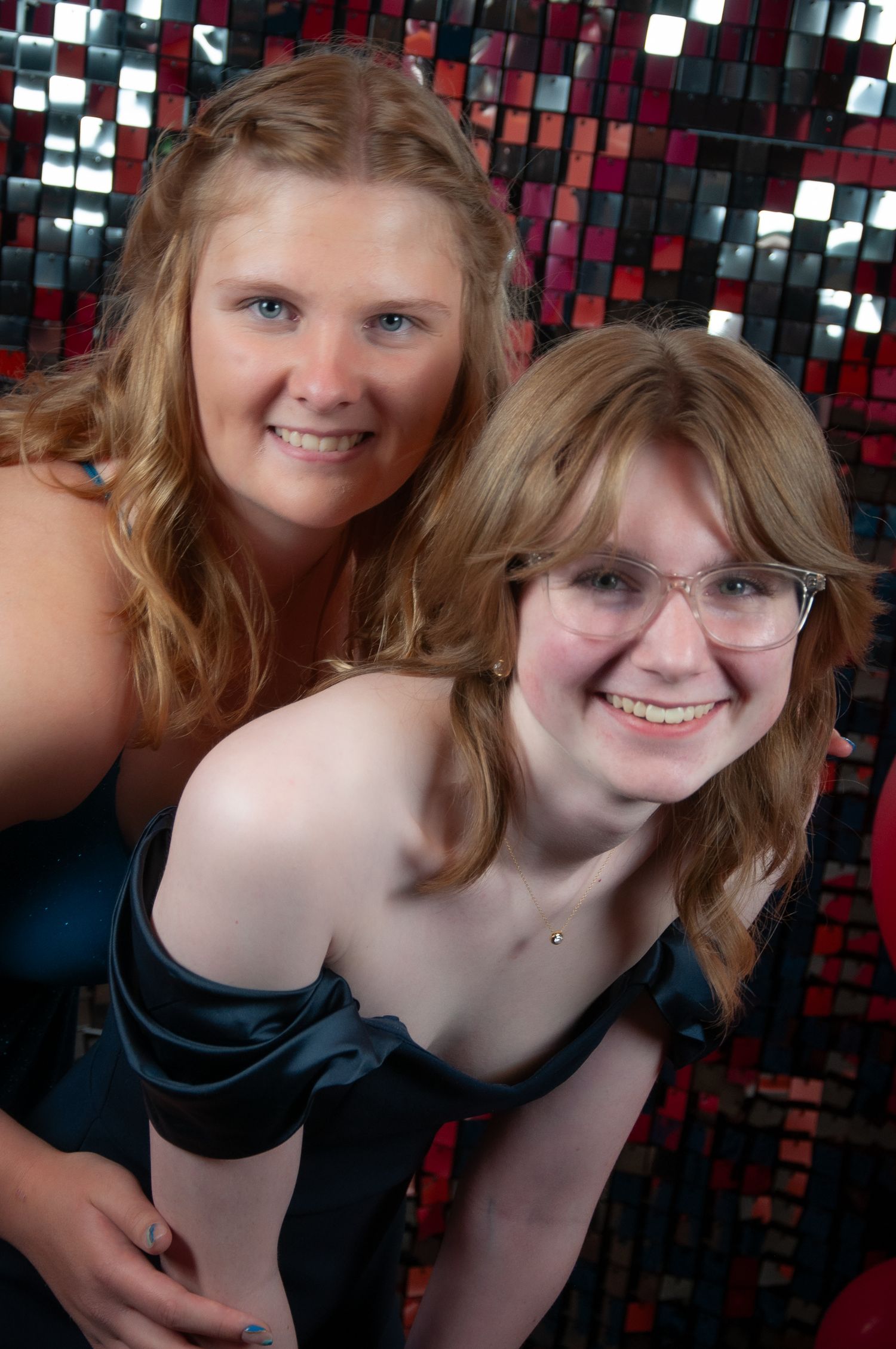 2 young ladies pose together in front of a glittered wall