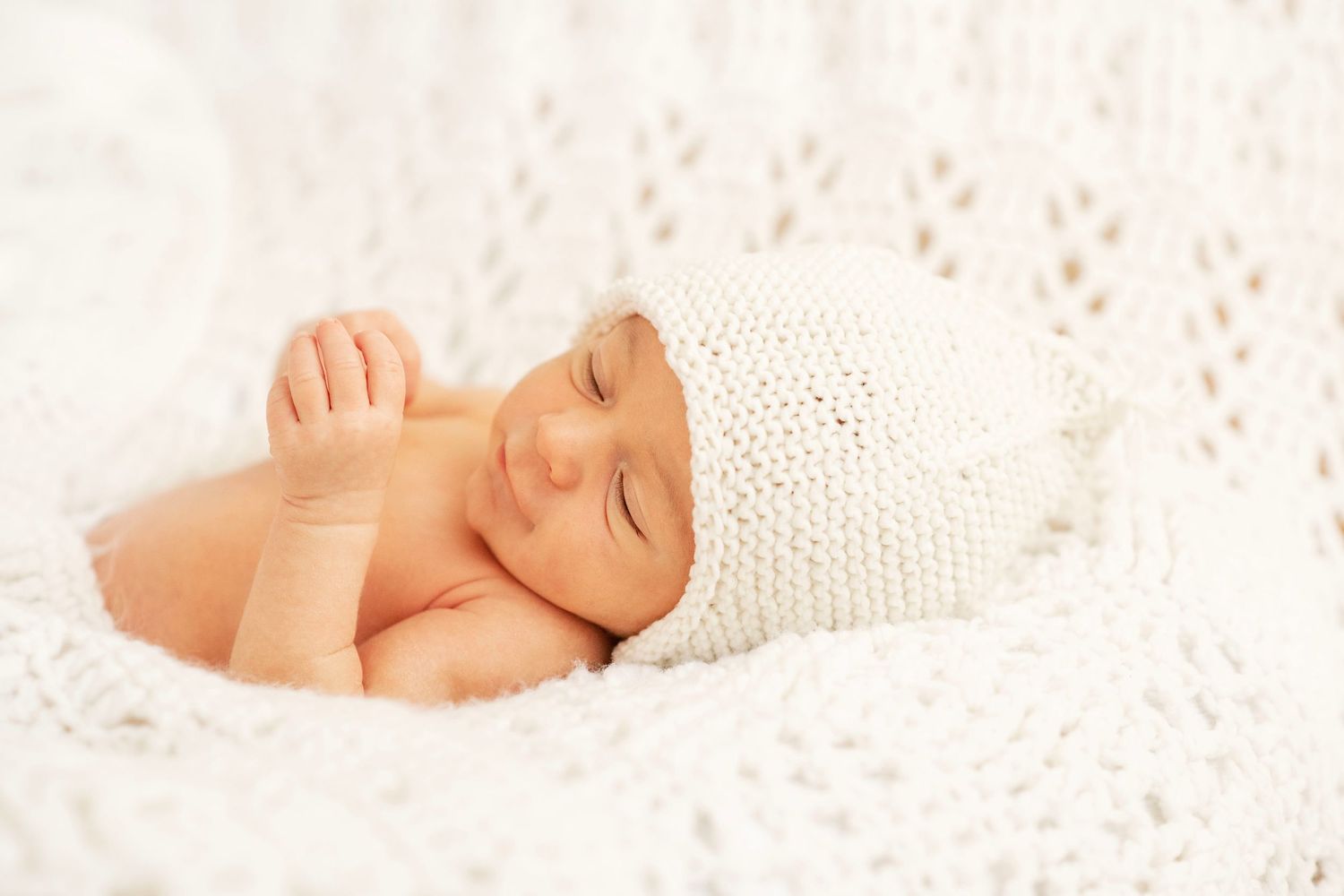 newborn baby photo. sweet closeup of newborn boy in white knit hat on knit blanket. Bright, clean stunning photo professional lighting