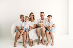 Happy family of six posing together on a white couch in a bright studio portrait.
