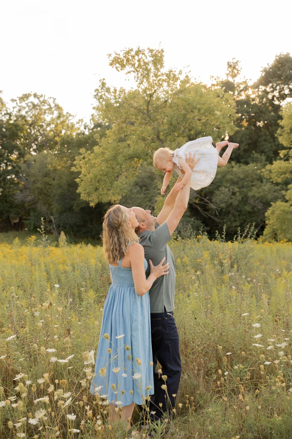 Couple air planing their toddler daughter into the air together in a wildflower meadow at sunset at bear creek in Rochester michigan