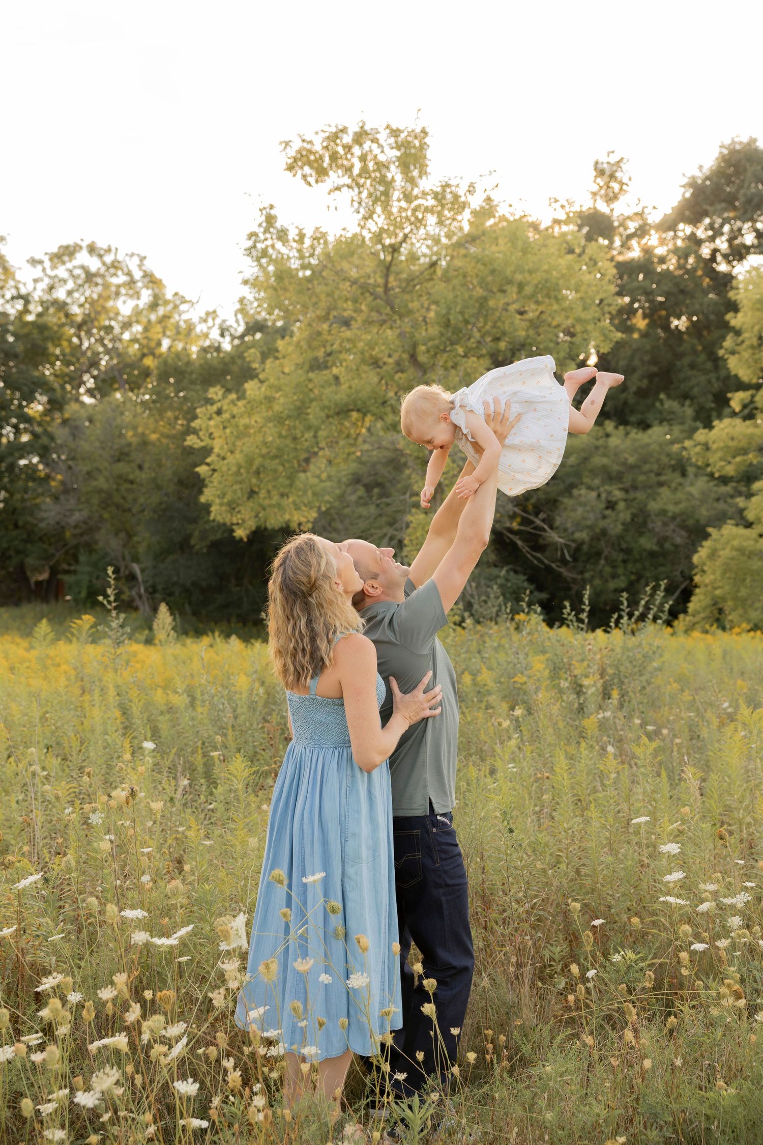Couple air planing their toddler daughter into the air together in a wildflower meadow at sunset at bear creek in Rochester michigan