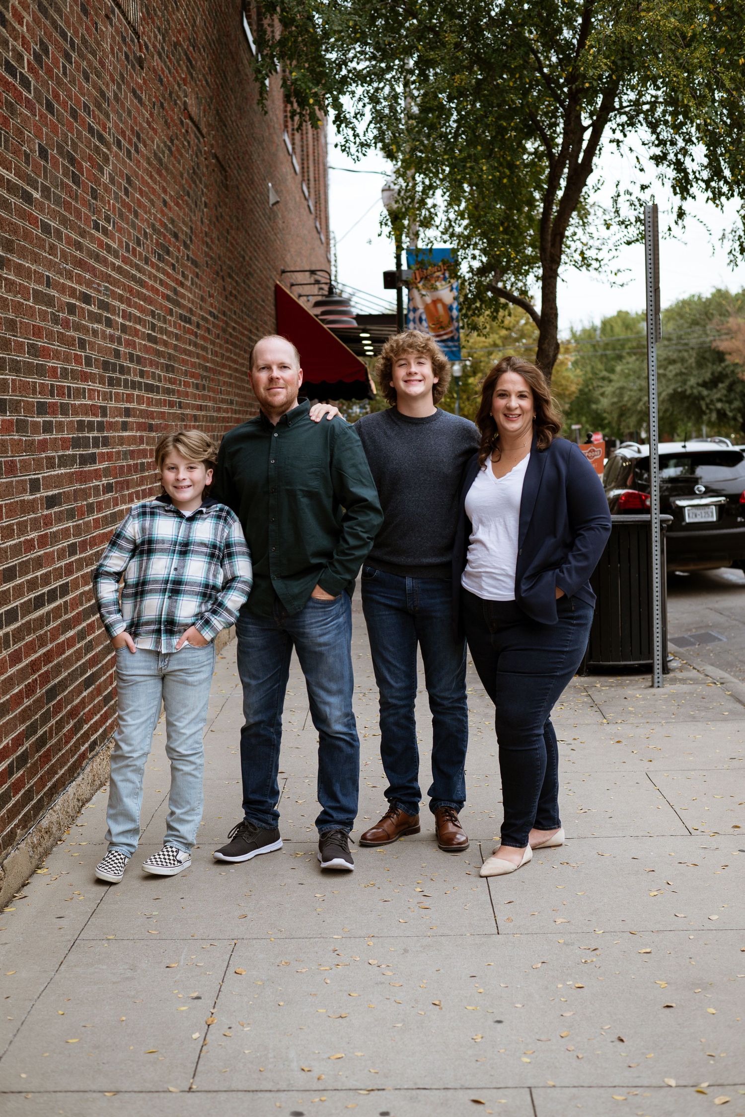 A group poses casually against a brick wall on an urban sidewalk.