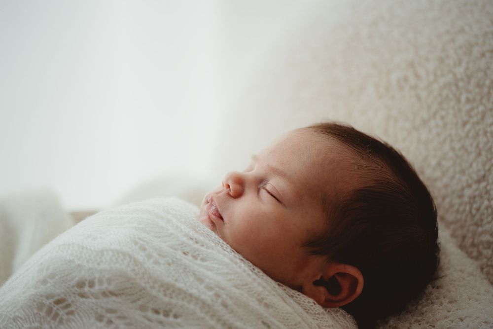 A sleeping baby lies peacefully on soft white bedding in a series of connected photos.