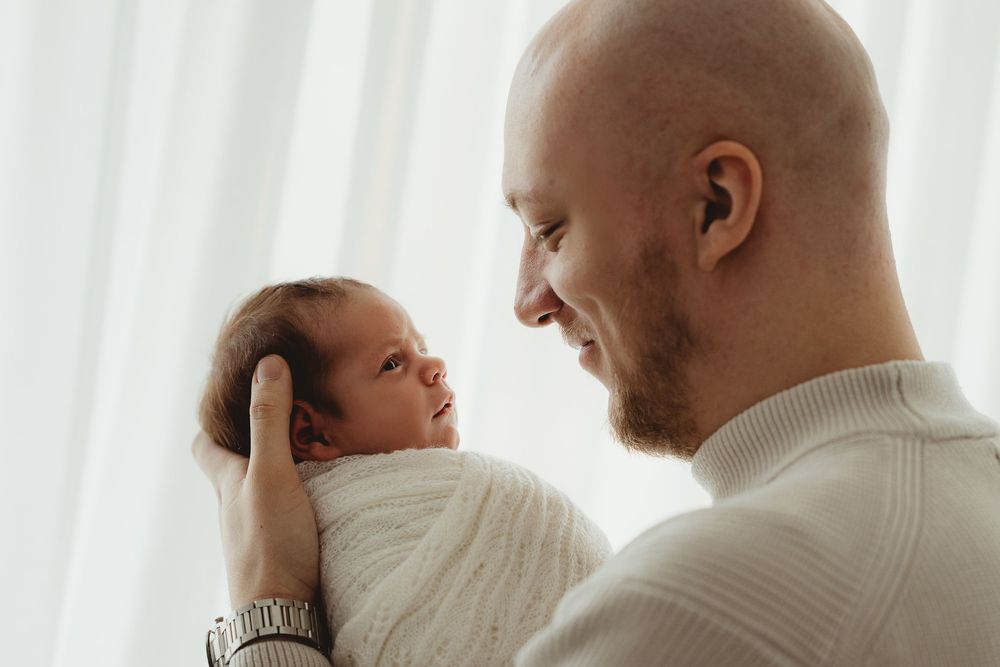 Four connected images show tender moments between a parent and baby wearing matching cream-colored sweaters.