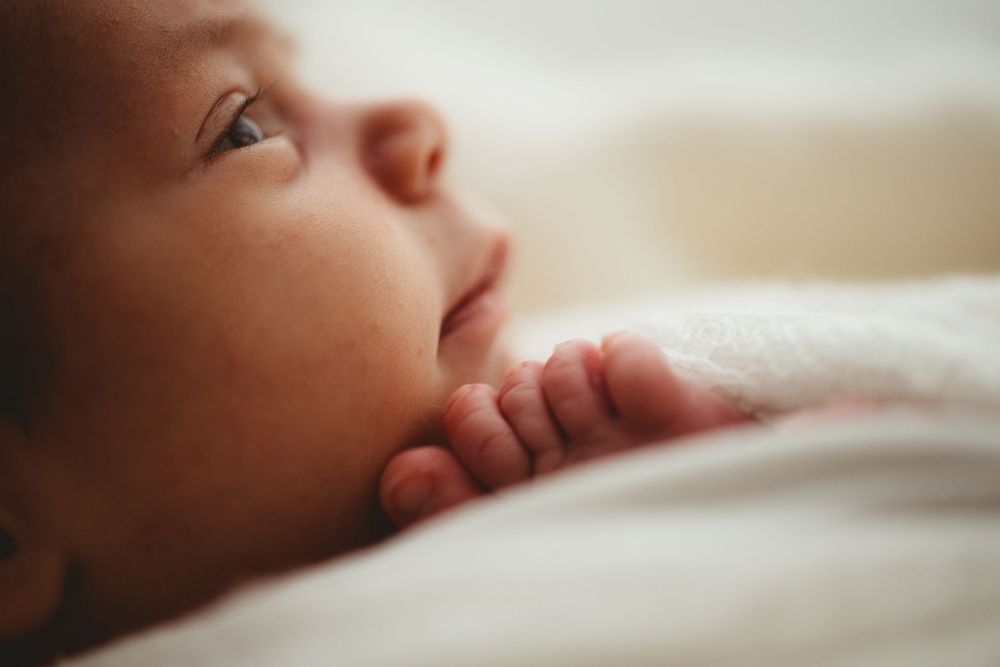 Close-up view of a baby's peaceful face resting on soft white bedding in natural light.