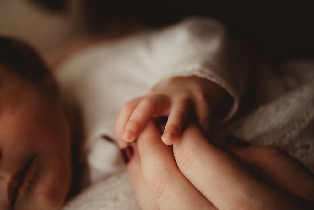 Close-up of a tiny baby hand grasping an adult's finger while resting on soft white fabric.