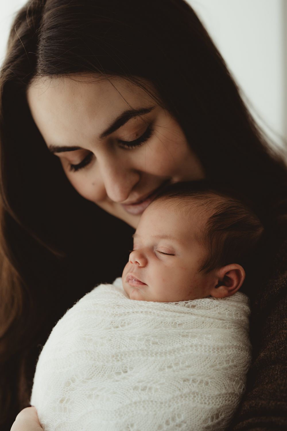 A tender moment captured in black and white as a parent holds a sleeping baby wrapped in a cozy white knit blanket.