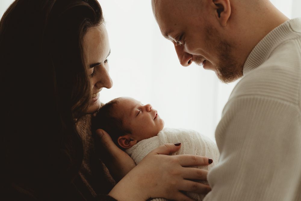Tender black and white photo series showing intimate moments between parents and their newborn baby in soft lighting.
