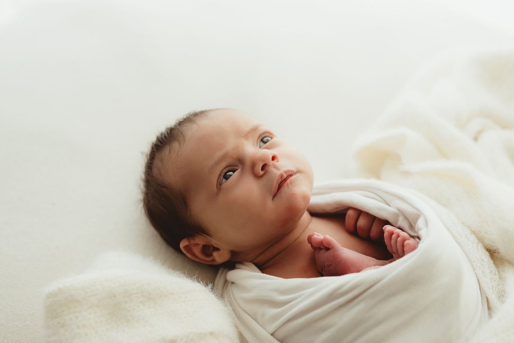 A newborn baby wrapped in white fabric lies peacefully on a soft surface.