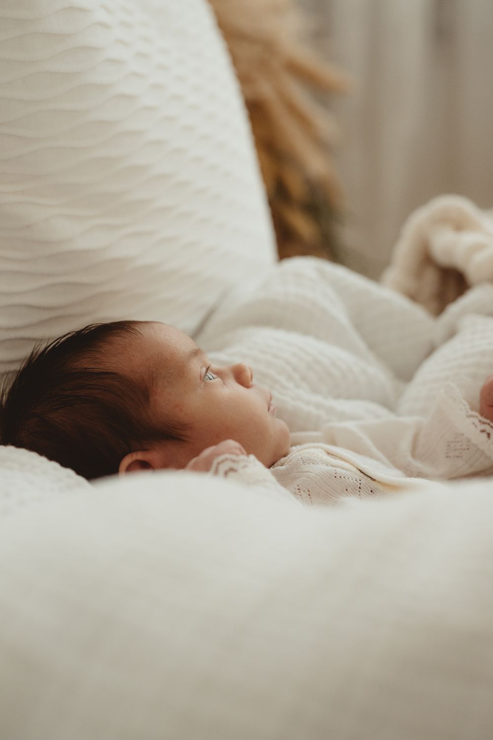 A sleeping newborn baby rests peacefully on soft white bedding in a series of gentle profile portraits.