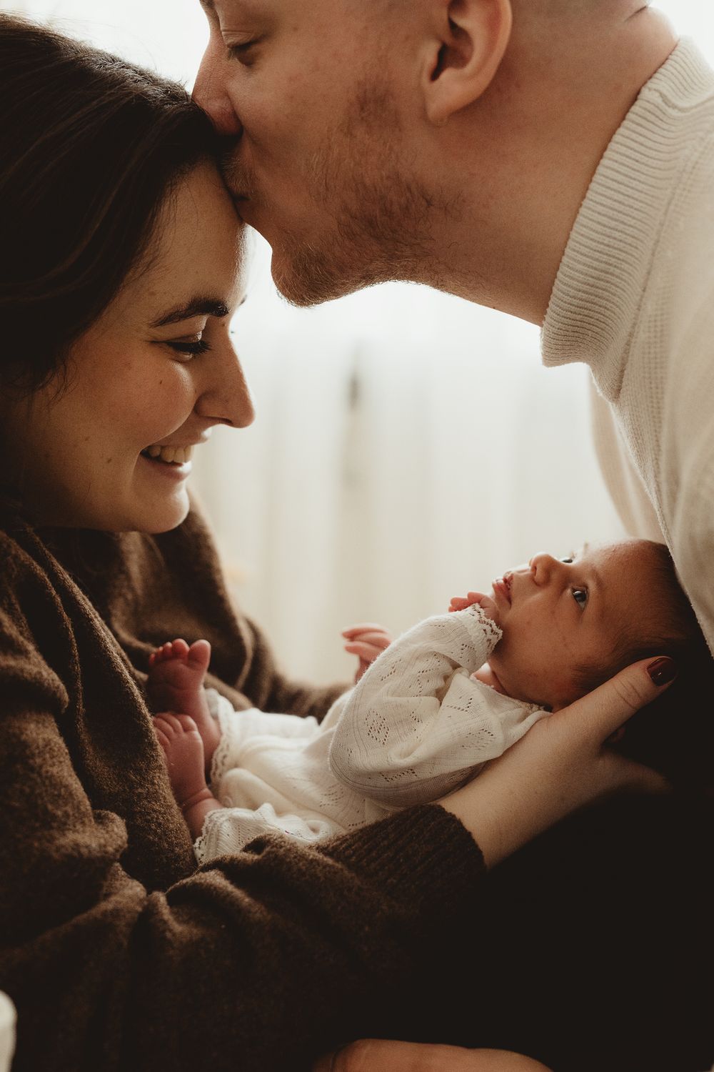 Intimate family moment as parents share tender interaction with their newborn baby in warm lighting.