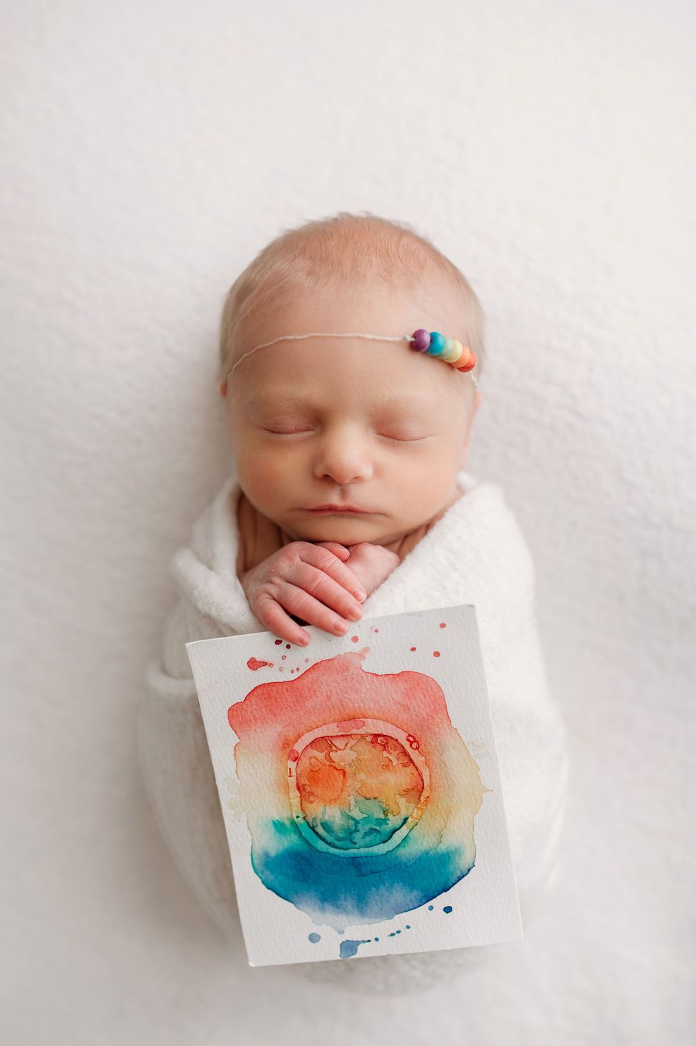 Rainbow baby girl holding rainbow painting of themself as an embryo