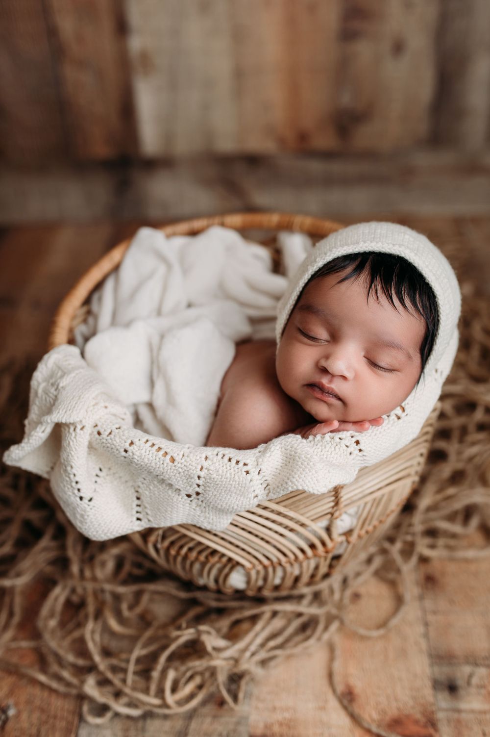 newborn baby in bonnet with basket in white and rattan on wood
