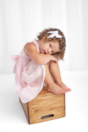 Photo of girl with curly hair in pink dress and bow hugging her knees.
