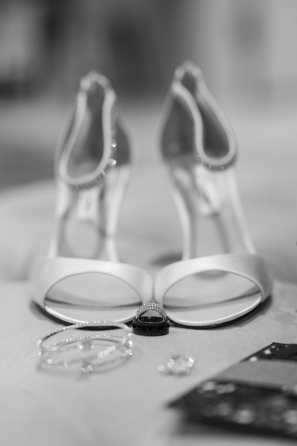 Wedding accessories including white heels, rings and jewelry arranged on light surface.