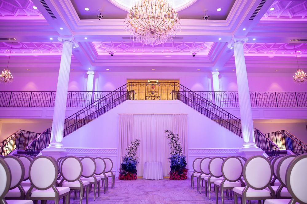 Elegant ballroom with crystal chandelier and white chairs set up for wedding ceremony.