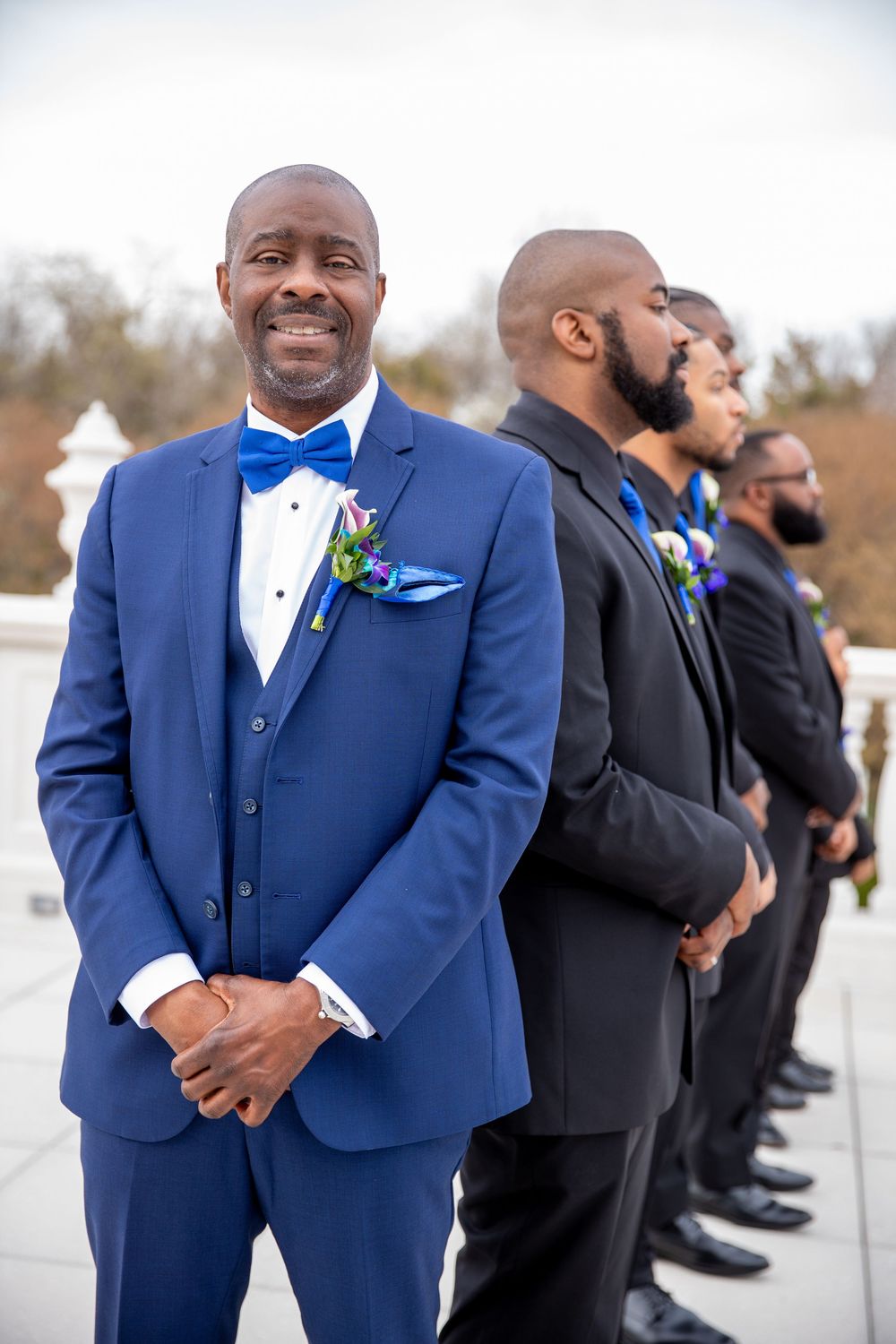 Wedding party in blue and black tuxedos standing outdoors.