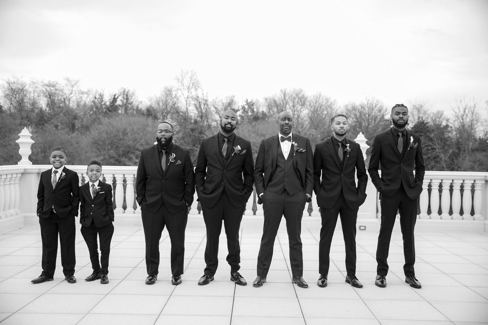 Groomsmen pose for a black and white photo on an outdoor balcony.