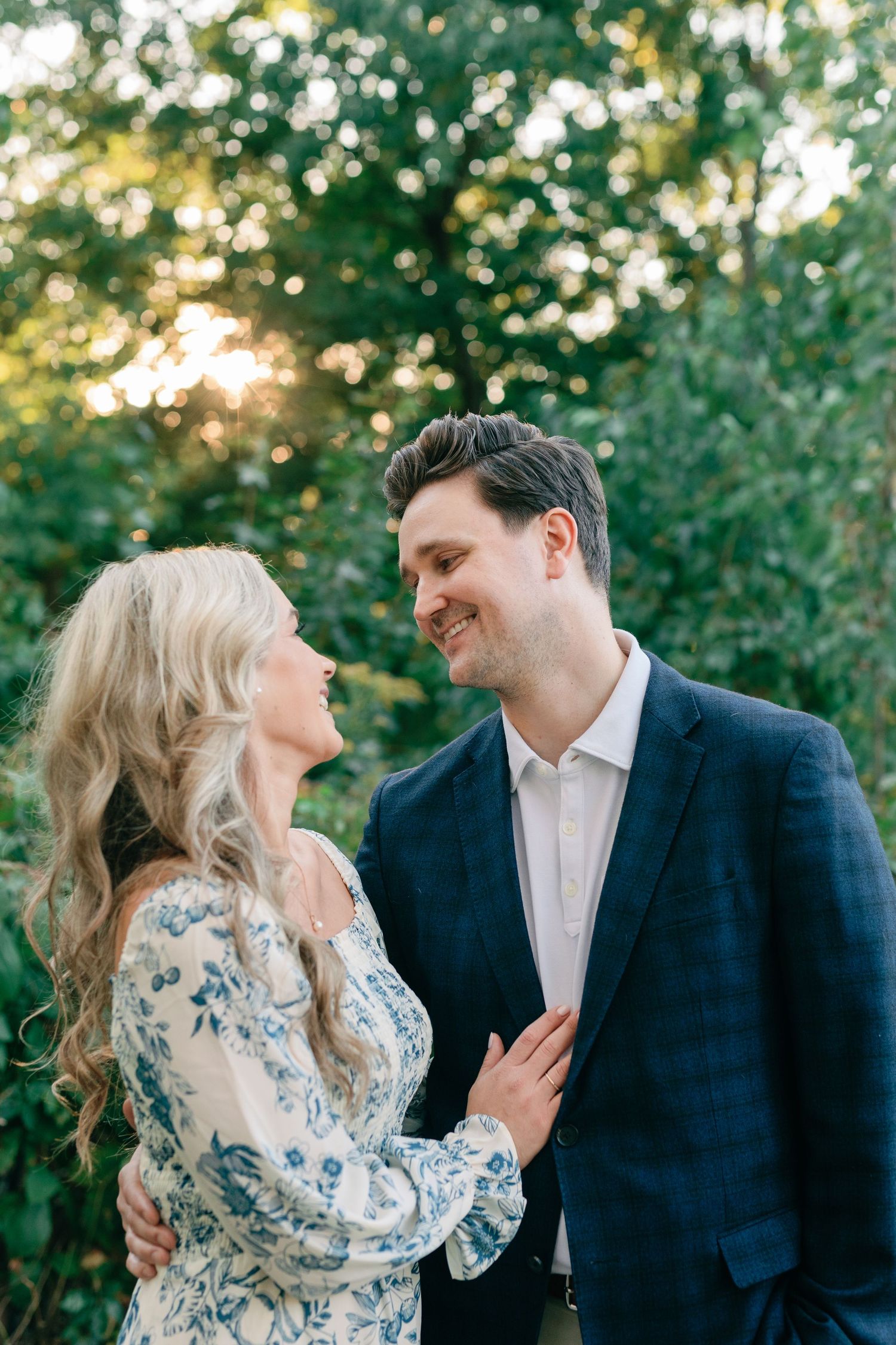 A couple smiles at each other in High Park. The man's arm is around the woman's waist, and her hand rests on his chest.
