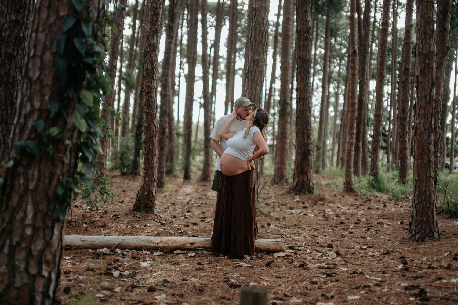 Couple sharing a tender moment while holding an ultrasound photo against a bright sky.