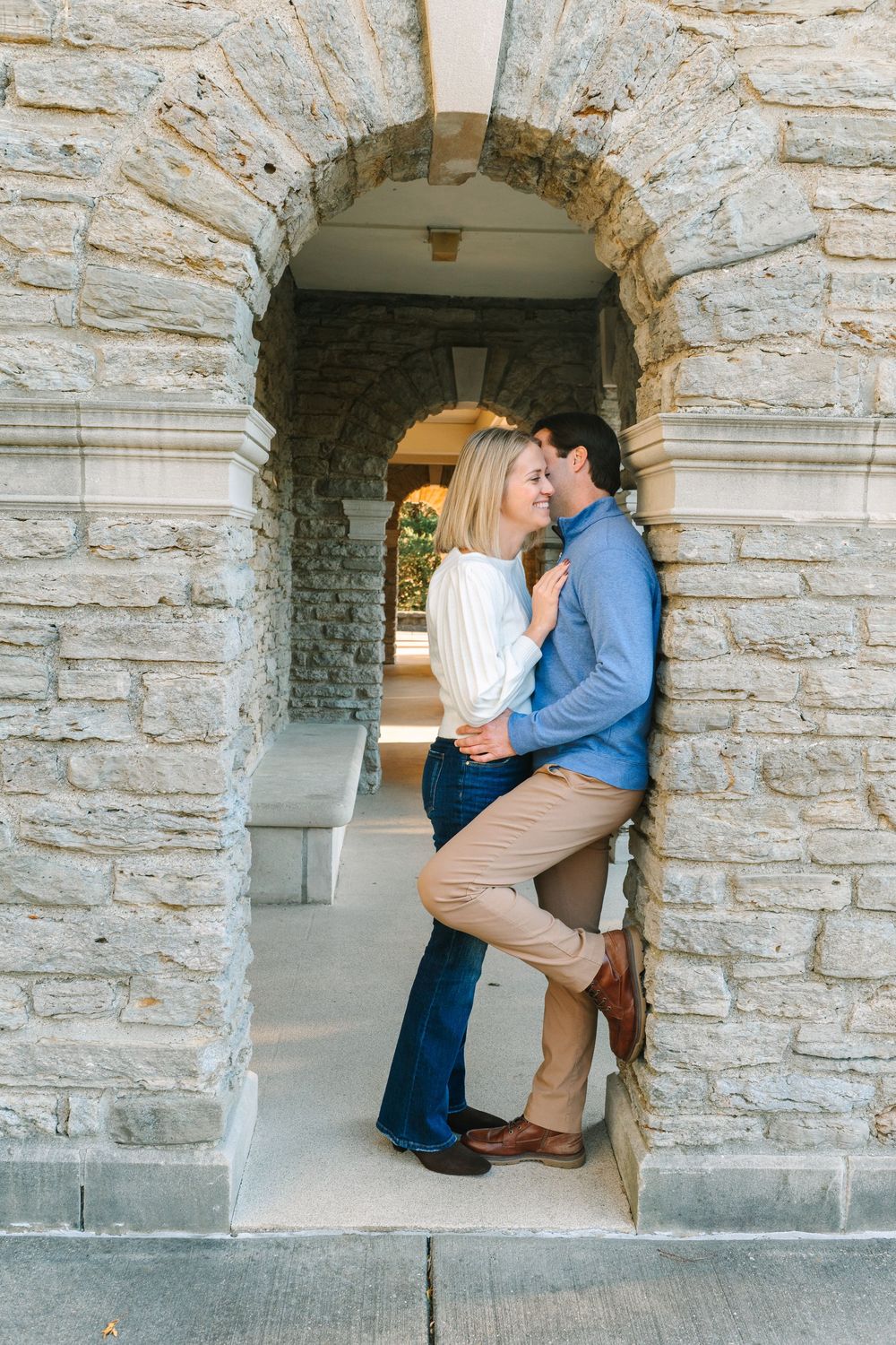 A couple embraces in a sunlit autumn field wearing neutral colored sweaters.