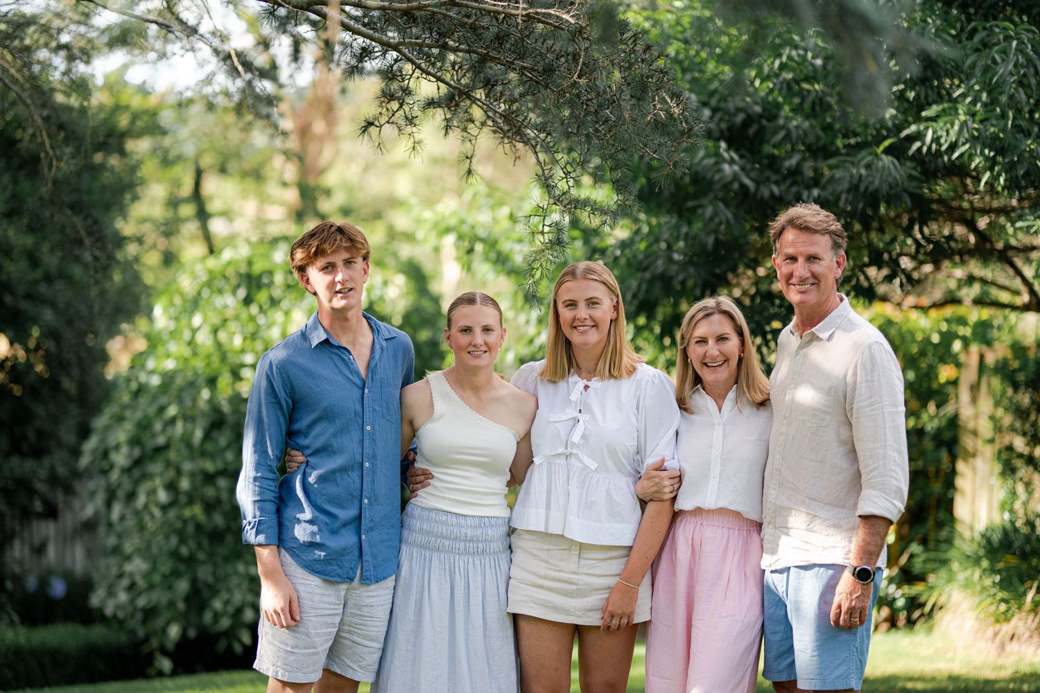 A wedding party is walking outdoors in a field. The bride and groom are in the center, with bridesmaids and groomsmen on either side.