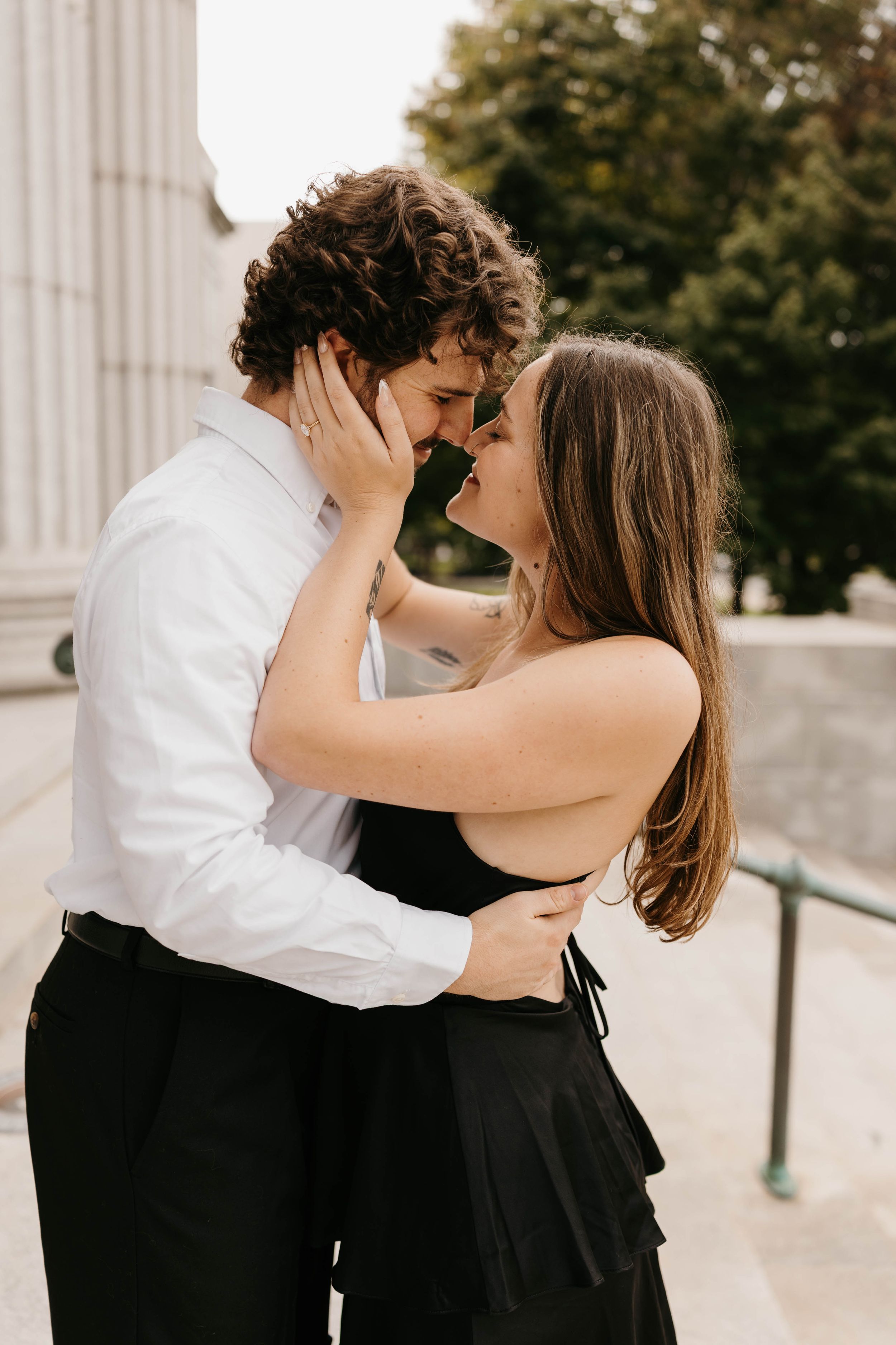 Young couple shares a passionate kiss on outdoor steps near classic stone columns in urban setting.