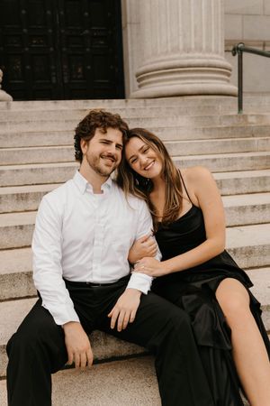 Smiling couple sitting closely together on stone steps during classic engagement portrait session.