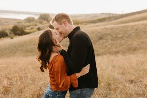 Romantic couple nearly kissing in golden grass field, woman in orange top and man in black shirt.