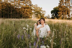 Couple hugging and smiling in wildflower meadow with warm sunset light and forest behind them.
