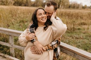 Happy couple embraces and laughs together by wooden fence in autumn field at golden hour.