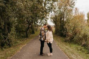 Couple sharing a tender kiss on a tree-lined path during autumn engagement session.
